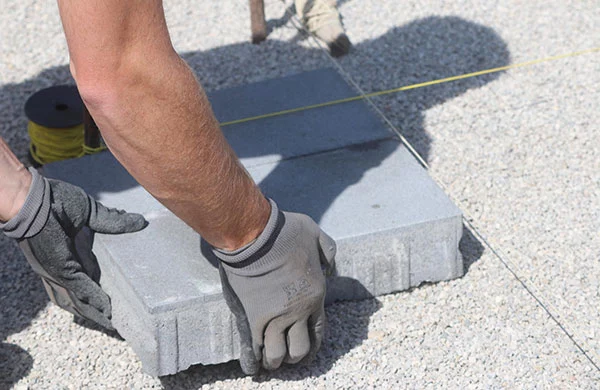 Hände mit Arbeitshandschuhen verlegen Pflastersteine